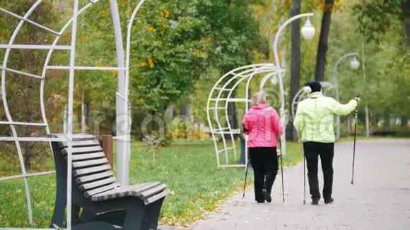 穿着夹克衫的老妇人在斯堪的纳维亚人散步的秋天公园的人行道上散步从后面看视频的预览图