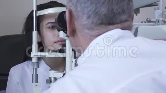 一位年轻漂亮的女士坐在诊所里做眼科检查她正坐在医生面前穿着白色的医用外套看着验眼机视频的预览图