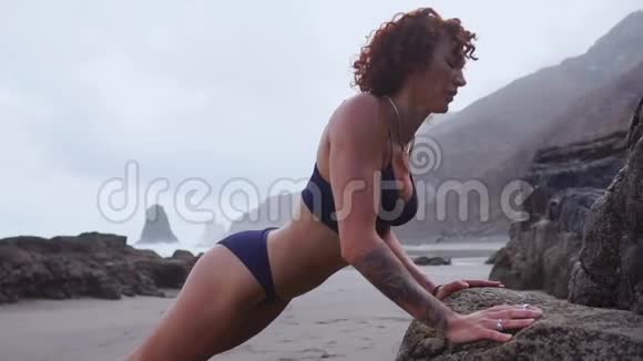 女运动员在一个美丽的海滩上训练时从岩石上进行挤压视频的预览图