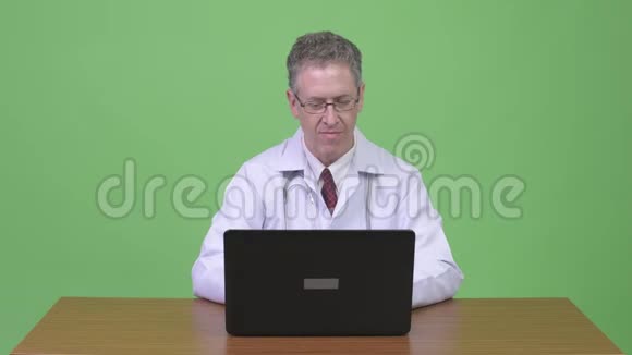 快乐的成熟男人的画像医生一边用笔记本电脑对着木桌思考视频的预览图