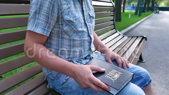 夏天阳光明媚的一天人们手里拿着圣经坐在公园的长凳上视频的预览图