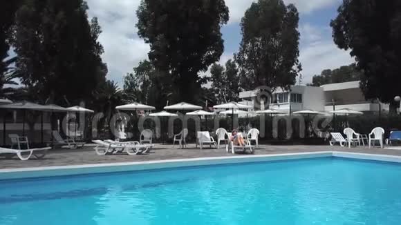 从顶部可以看到一个女人穿着蓝色泳衣在酒店别墅或别墅的游泳池旁的休息室里打日光浴视频的预览图
