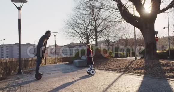 女儿亲她爸爸骑着赛格威气垫船现代未来运输技术积极的家庭公园人行道视频的预览图