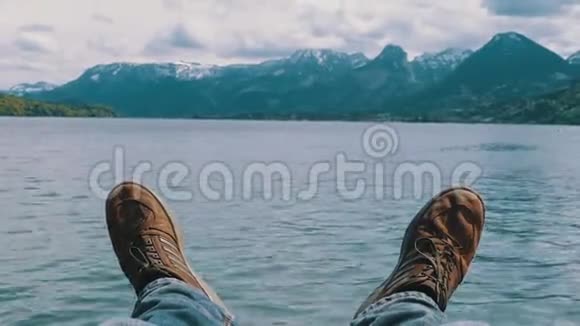 人的双腿在一个山湖和白雪覆盖的山脉的背景上视频的预览图