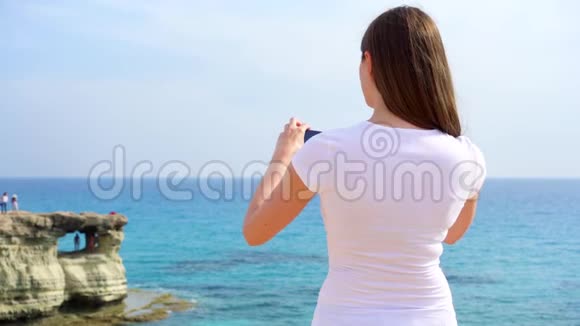 年轻女子在手机上慢动作拍摄蓝色地中海从后面看视频的预览图