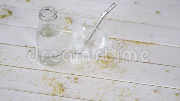 带钛吸管的水晶水玻璃和带沙木桌上的瓶子视频的预览图