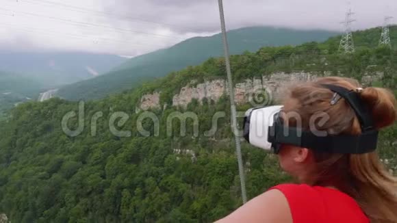 穿着红色衣服的金发女郎和虚拟现实的眼镜把她的手放在绿树林山的背景下视频的预览图