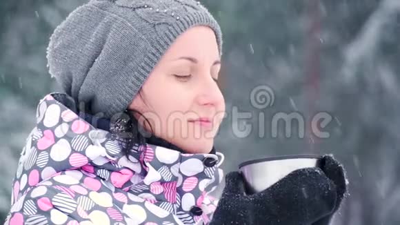 一个女孩站在寒冷的森林或公园里在一个下雪的冬天一位女游客从杯子里喝热茶旅游业和旅游业视频的预览图