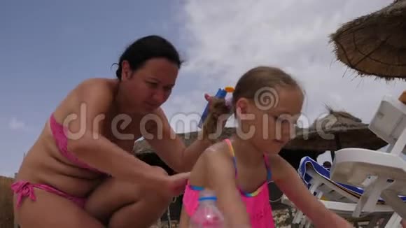 年轻的妈妈在夏天的海滩上给女儿涂防晒霜视频的预览图
