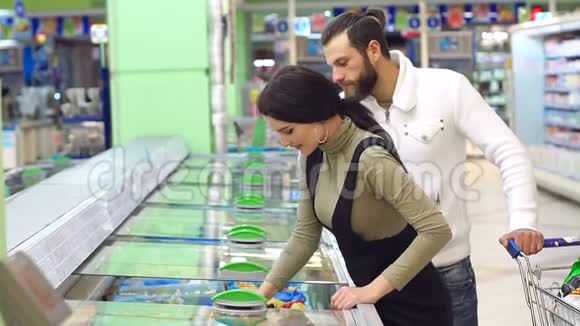 一对年轻夫妇站在冰箱附近的超市里买冷冻浆果视频的预览图