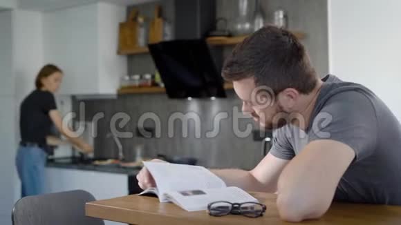 女人早上正在为心爱的丈夫做早餐男人坐在桌子旁看书视频的预览图