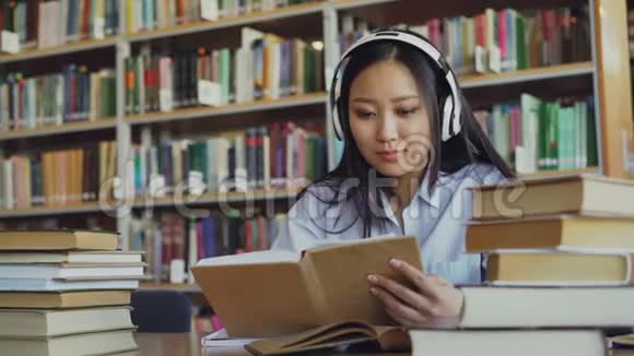 相当积极的亚洲青少年学生头戴耳机听音乐正坐在大图书馆的桌子旁视频的预览图