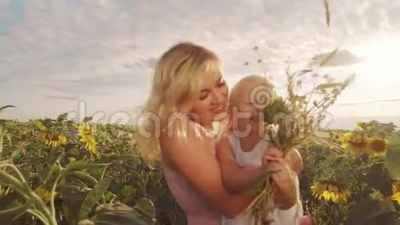 一个带着一个小孩子的年轻女人站在一大片向日葵的中间美丽的日落时光A视频的预览图