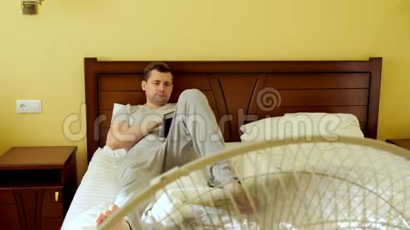 一个男人躺在床上看书夏日炎炎风扇工作视频的预览图