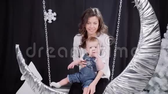 一位年轻的母亲带着一个小儿子骑着一个月的秋千圣诞快乐节日快乐视频的预览图