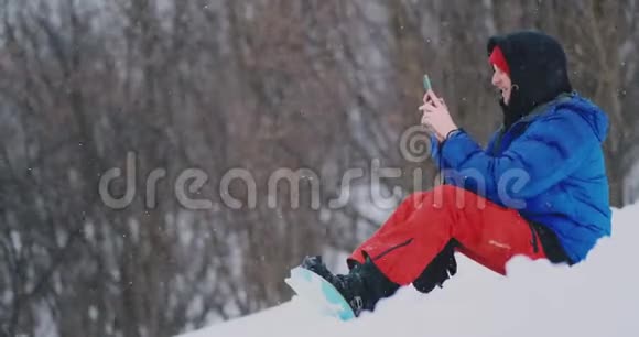 男性滑雪者坐在雪地上拍照打电话美丽的风景胜地为社交网络服务视频的预览图