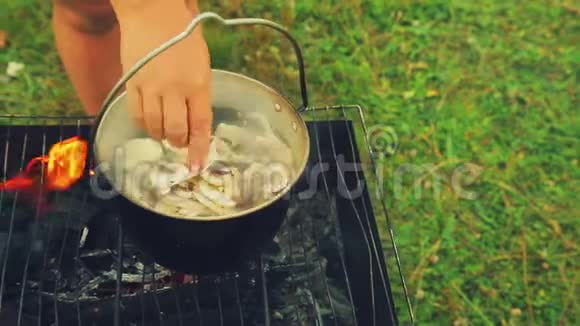一个女人手把蘑菇放在火上的水壶里煮汤视频的预览图