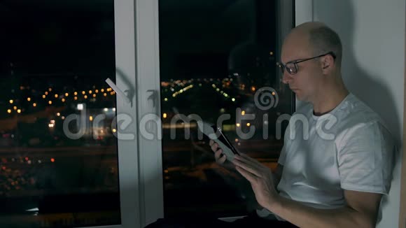 戴眼镜看电子书晚上坐在窗台上的中年人视频的预览图