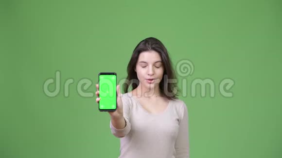 年轻的美女在绿色背景下展示手机时神情震惊视频的预览图