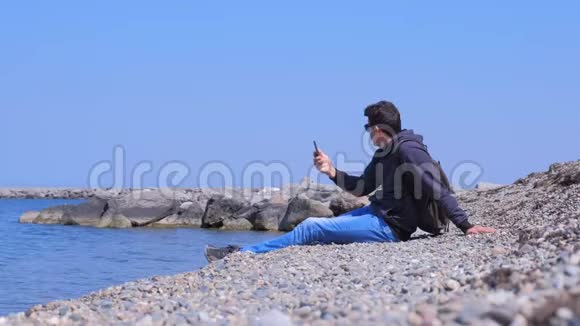 男人在他的智能手机上谈论视频聊天坐在海边度假视频的预览图