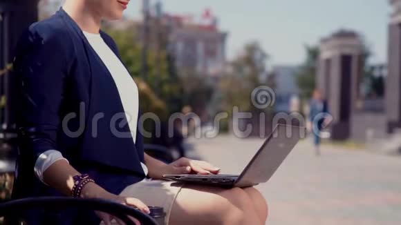 一个年轻的商人坐在一个公园的长凳上一条有办公楼的城市街道被阳光照亮一个女孩抱着视频的预览图