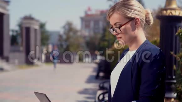 一个年轻的女孩在她的笔记本电脑上从事一项商业项目她坐在一条城市街道上远处的人是视频的预览图
