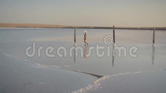 苗条的女孩享受日落漫步在盐湖的木制盐柱之间视频的预览图