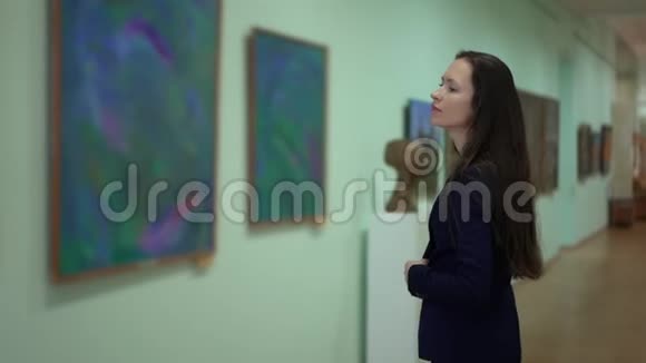 优雅美丽的女人看着现代艺术博物馆里的照片展览的艺术绘画作品视频的预览图