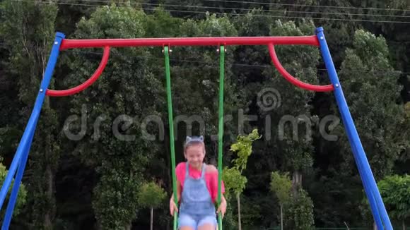 微笑快乐的八岁女孩在秋千上荡秋千户外在公园里夏天炎热的一天在度假小可爱视频的预览图
