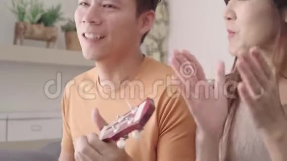 亚洲夫妇在家里的客厅里一起弹吉他和唱歌甜蜜的夫妇享受爱情的时刻视频的预览图