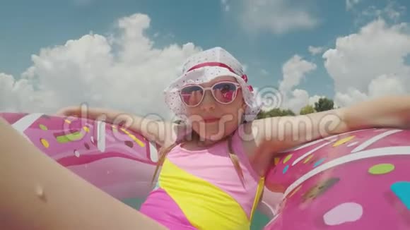 在海滨度过一个愉快的假期一个女孩坐在凉爽的巴拿马戴着太阳镜在粉红色的充气圆圈里航行视频的预览图
