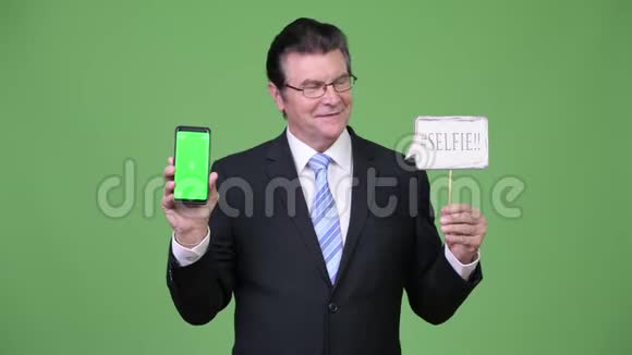 高级帅哥商人带着手机和自拍纸标志视频的预览图