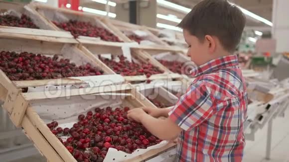 有趣的小男孩在超市的家庭购物中从盒子里摘樱桃视频的预览图