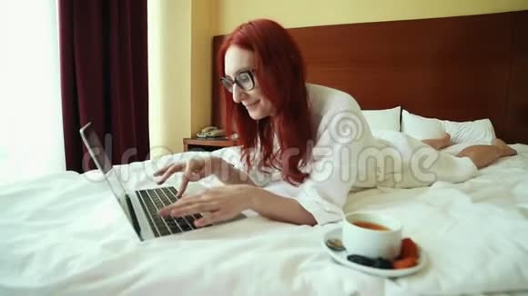 一个姜黄色的女人躺在床上和一个笔记本电脑自由职业视频的预览图