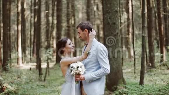 新娘和新郎拥抱在一起微笑着站在茂密的松林乡村婚礼上视频的预览图