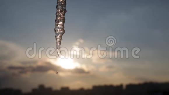 巨大的长冰柱在城市的日落天空靠近融化的水滴从冰柱中落下视频的预览图