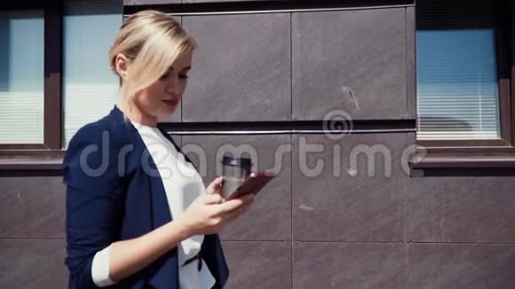 一位年轻的商人站在办公楼附近那里的窗户是可见的女孩看着智能手机视频的预览图