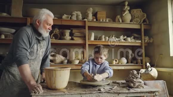 小男孩正在爷爷的工作室里泥塑制品而他关心的老爷爷正站在他身边视频的预览图