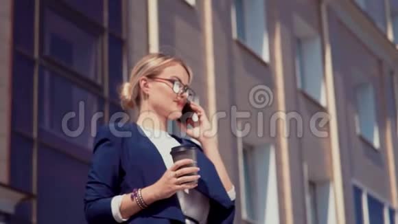 这位商人站在办公楼附近她打电话拿着一杯咖啡她的右手视频的预览图