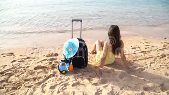 美丽的女人坐在阳光明媚的海滩上提着一个手提箱视频的预览图