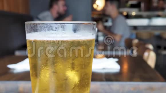 在一家有人用餐的餐厅里刚倒出的一杯淡啤酒在玻璃顶上冒泡视频的预览图