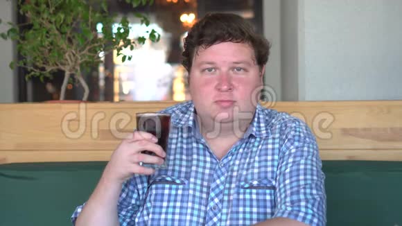 胖子拿着一杯碳酸软饮料可乐坐在咖啡馆里饮料和健康视频的预览图
