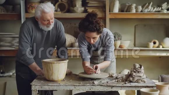 关心爷爷的经验丰富的陶工正在教永女孩如何在陶工车轮上使用粘土陶器家庭视频的预览图