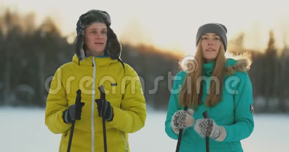 在日落时分的冬季森林里一男一女一滑雪看着大自然的美景和慢镜头视频的预览图