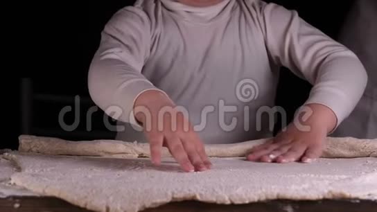 一个黑背景的小男孩帮助他父亲的厨师准备面团为比萨饼面包蛋糕和视频的预览图