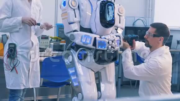 两名工程师正在修理一个类似人类的机器人视频的预览图