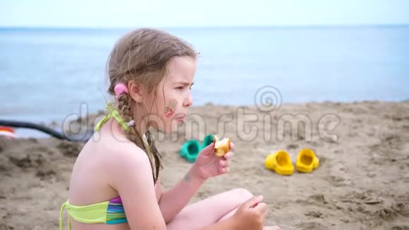女孩坐在靠近水的沙岸上吃了一个面包夏日炎炎家庭海上度假视频的预览图