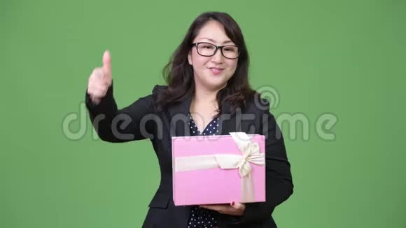 成熟美丽的亚洲女商人拿着礼品盒指着相机视频的预览图