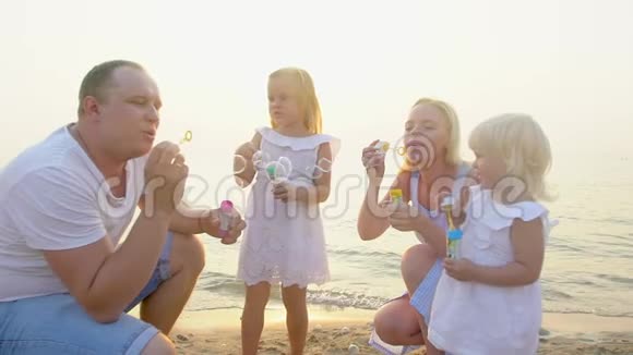 快乐的四口之家在美丽的日落中在海滩上玩肥皂泡快乐的度假时光慢慢地视频的预览图