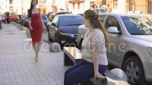 肥胖的女性艳羡地看着从街上经过的苗条美丽的女士饮食视频的预览图